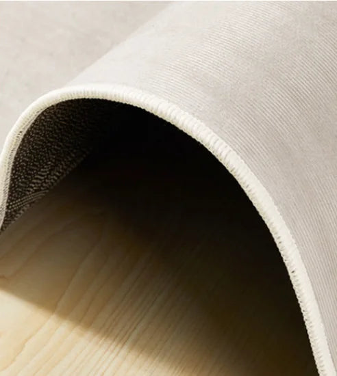 Close-up of a beige rug with a textured edge on a light wooden floor.