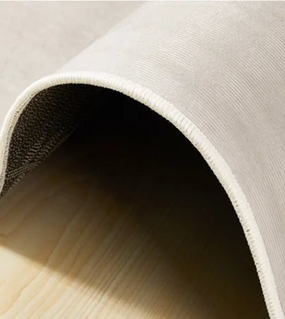 Close-up of a beige rug with a textured edge on a light wooden floor.
