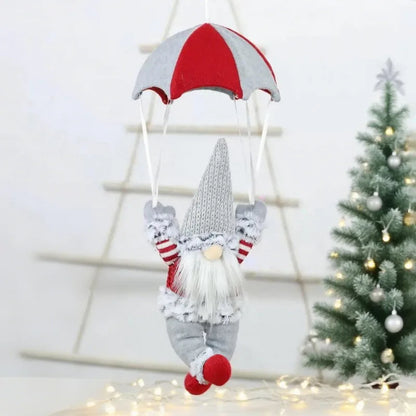 Decorative gnome with a red and white striped hat hanging from a string, with a Christmas tree in the background.
