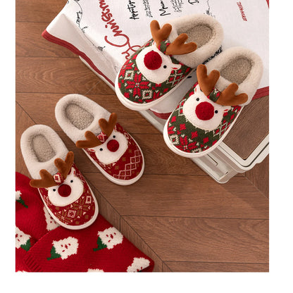 Pair of reindeer-themed slippers on a wooden floor with a towel in the background.