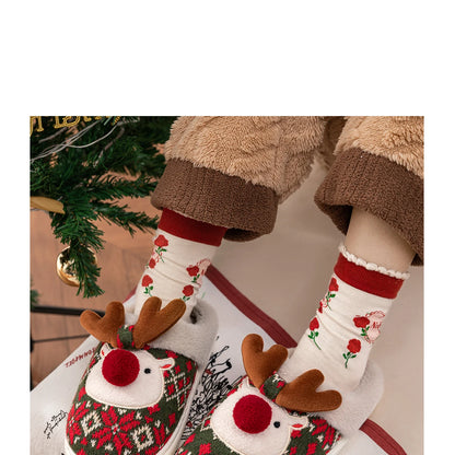 Person wearing festive socks with reindeer design next to a Christmas tree.