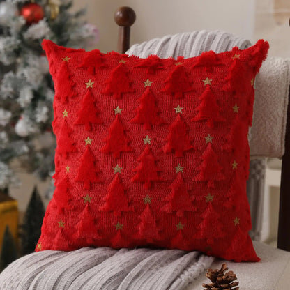 Red knitted pillow with Christmas tree pattern on a chair with a blurred Christmas tree in the background.