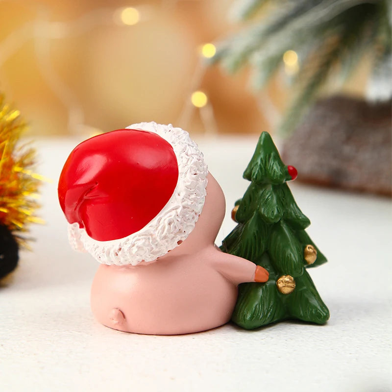 Decorative figurine of a pig wearing a Santa hat next to a small Christmas tree with a blurred festive background.