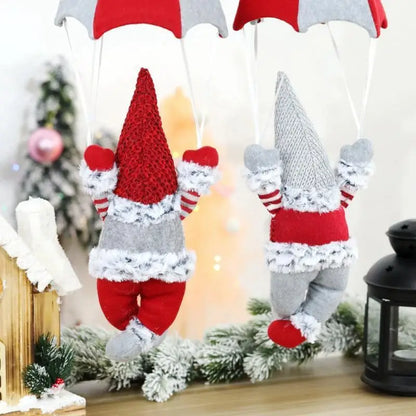 Two knitted gnomes in red and gray outfits hanging from an umbrella against a Christmas-themed background.