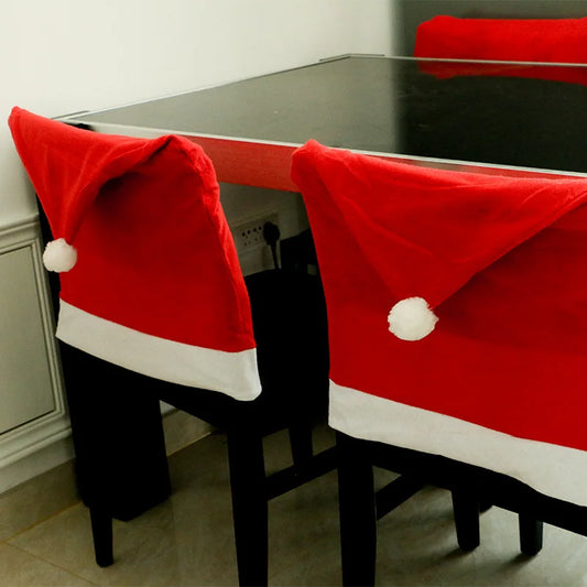 Two chairs with Santa hats draped over them in front of a glass table.