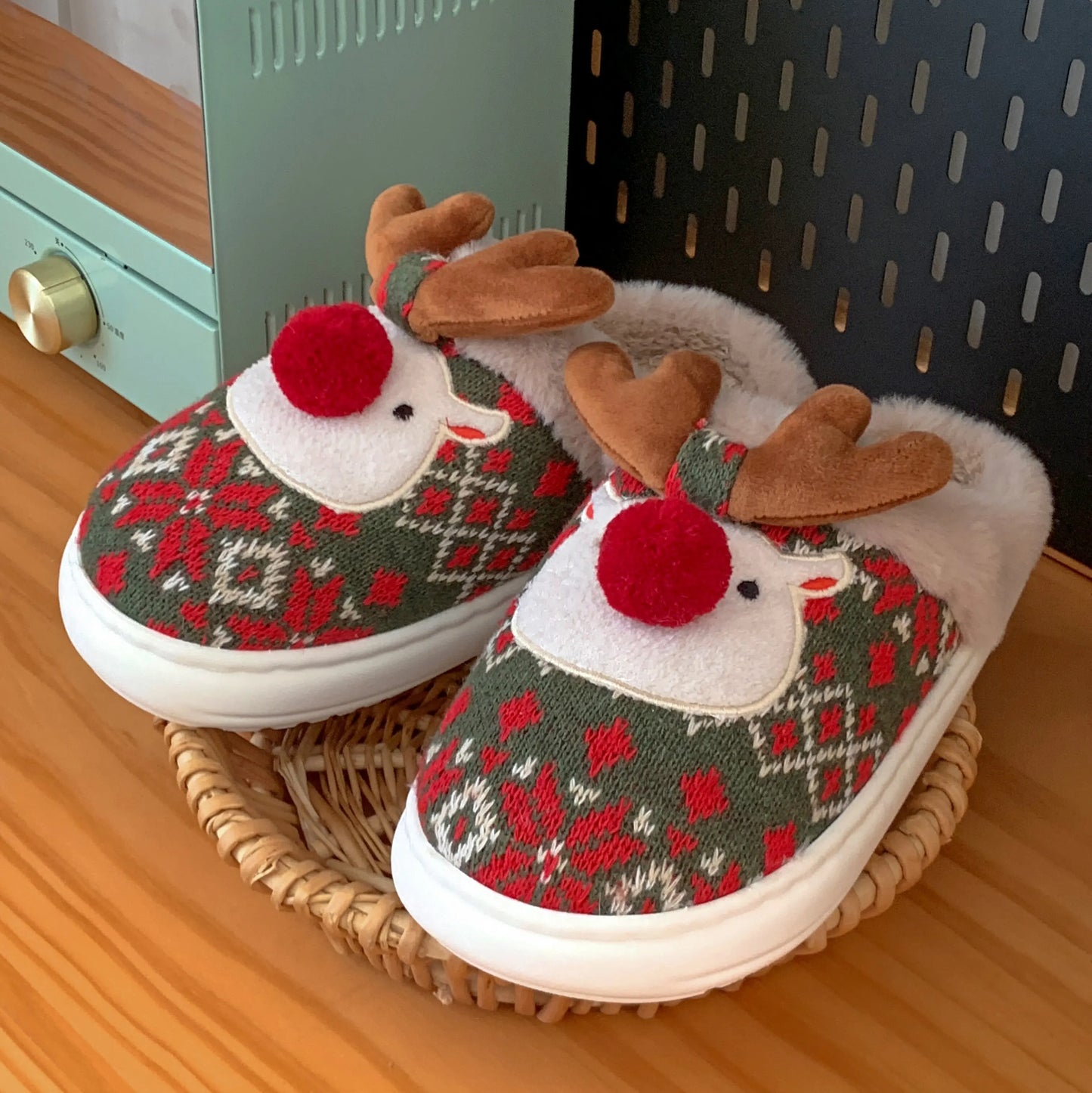 Pair of reindeer-themed slippers on a wooden surface with a wicker basket.
