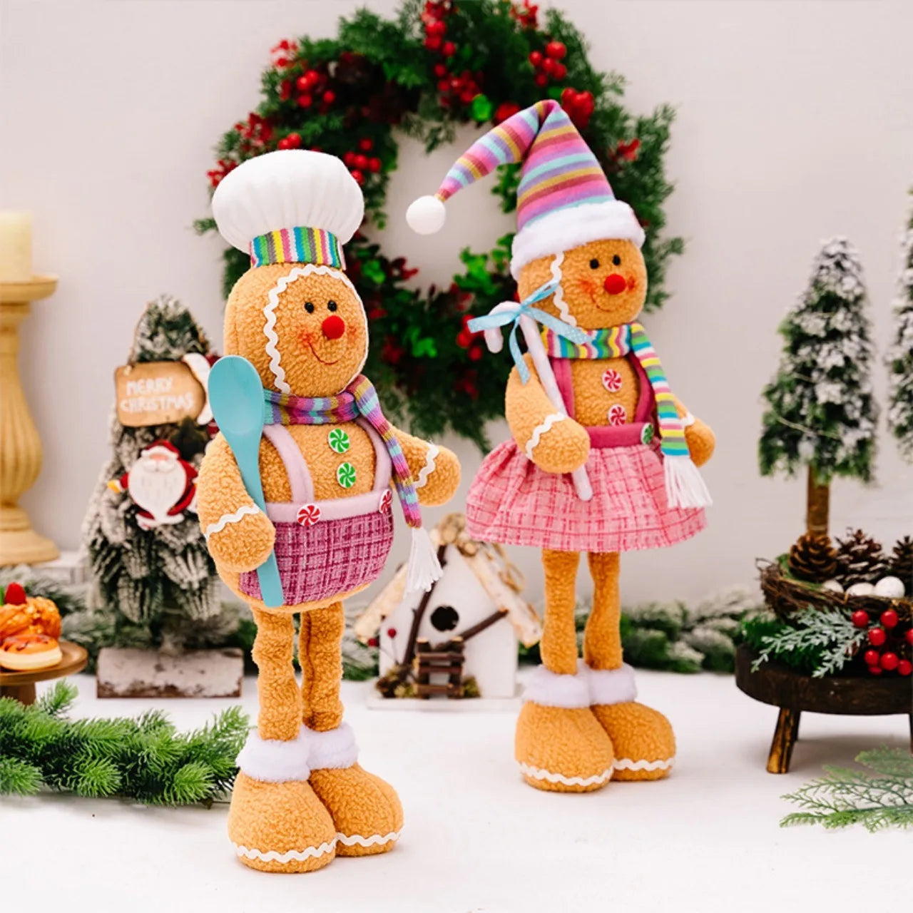 Two gingerbread-themed dolls in festive attire with a Christmas wreath in the background.