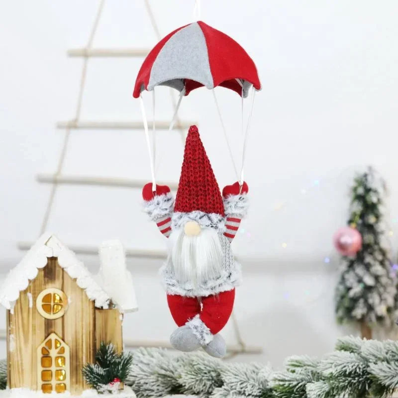 Decorative gnome with a red and gray hat in a festive setting with a small house and Christmas tree.