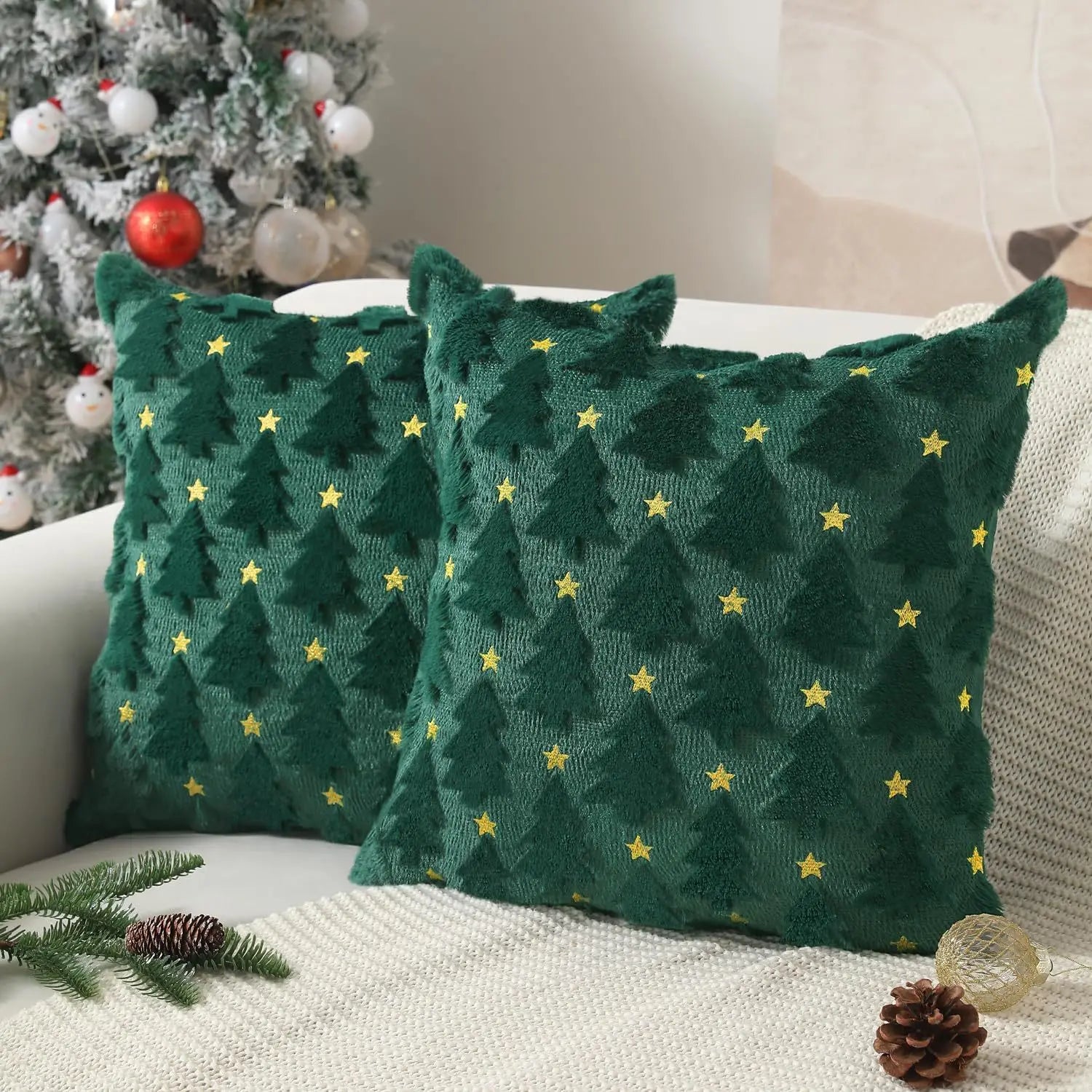Two green patterned pillows on a couch with a Christmas tree in the background.