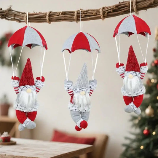 Three gnome ornaments with red and white striped parachutes hanging against a blurred indoor background.