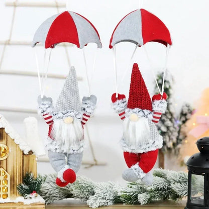 Two festive gnomes with red and white hats hanging on a branch with Christmas decorations in the background.