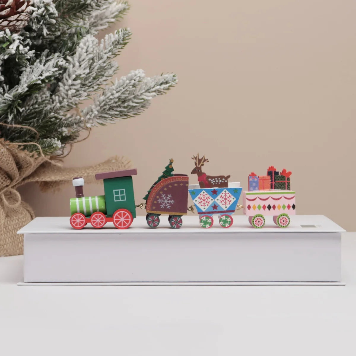 Decorative Christmas train set on a white platform with a Christmas tree in the background.
