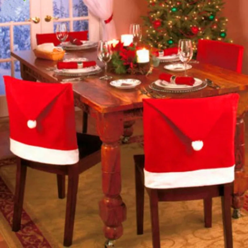 Dining table set for Christmas with Santa hats on chairs and a decorated tree in the background.